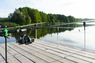 Carp fishing on beautiful blue lake with carp rods and rod pods in the summer morning. Fishing from the wooden platform.