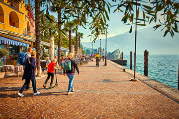 Tourists enjoying a walk around Lake Garda, colorful autumn in Riva del Garda surrounded by mountains, Trentino Alto Adige region, Lago di garda, italy