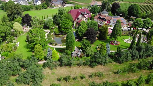 Beautiful park next to a hotel with vineyards in the background, aerial tilt up, Durbach, Germany