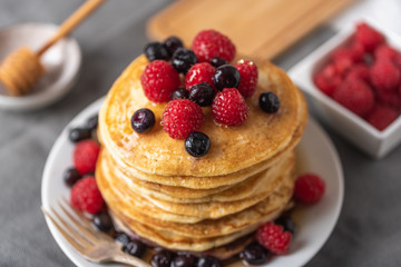 Sweet homemade pancakes with raspberries and blueberries on white plate.