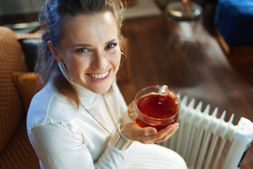 woman sitting on couch near oil radiator and holding tea cup