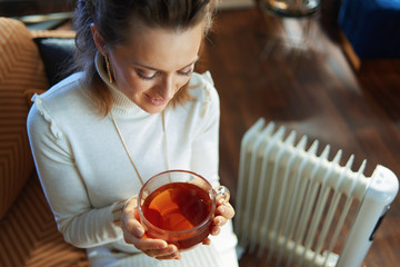 woman sitting on couch near oil radiator and drinking tea cup