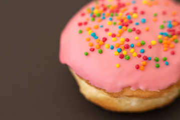 Delicious pink donut on black background close-up.