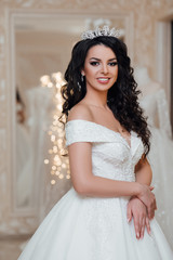 Pretty young excited woman is choosing a wedding dress in the shop. Beautiful girl with long wavy hair with a crown. Brunette model with makeup.