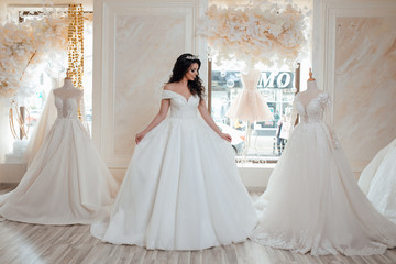 Naklejka premium Young happy bride looking for beautiful wedding dress, future bride came in designers salon, lovely woman dream about wedding. Beautiful bride choosing wedding dress in a wedding salon