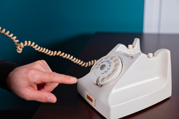 Phone old retro, old fashioned white telephone against green background, woman hand holding telephone cord in long exposure