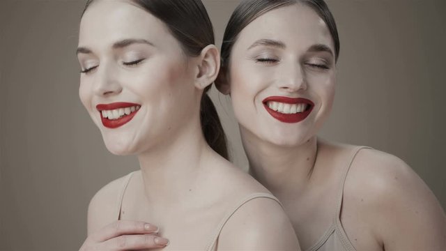 Red lipstick. Two twins girl with a nude makeup and red lips are smiling at the camera. Girls gossiping, joking. Nude make up.