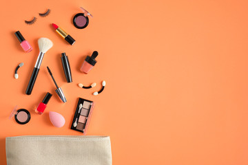 Makeup bag with cosmetic products spilling out on to a pastel orange color background. Flat lay,...