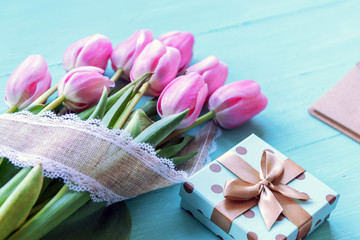 Pink tulips and gift in a box on turquoise wooden table. Women's day, Easter or spring concept.