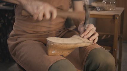 Traditional bespoke shoemaker nailing leather insole on wooden shoe last in workshop