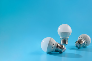 Three small white led energy saving led light bulbs on a blue background.