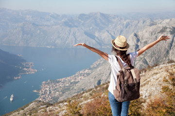 Traveler with backpack on mountain top. Happy woman with raised arms in amazing landscape. Girl tourist enjoying travel, adventure, freedom, vacation. Concept of solo female tourism, trip. Rear view. - obrazy, fototapety, plakaty