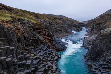 Studlagil canyon with basalt columns and blue water stream. Aerial drone view