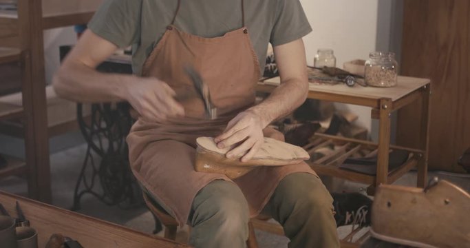 Traditional bespoke shoemaker nailing leather insole on wooden shoe last in workshop