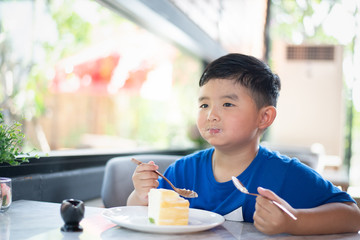 Asian boy eating cake in bakery shop or cafe.