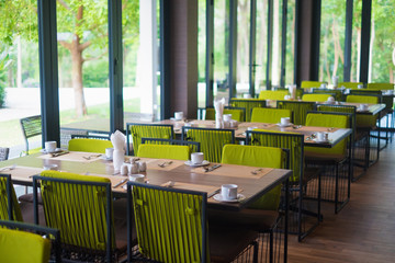 Empty restaurant part of hotel with table and armchair near windows and garden view.