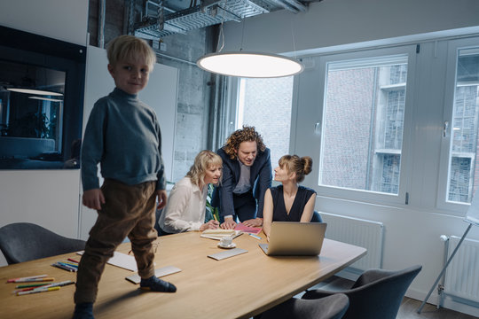 Boy Standing On Table In Office With Business Team Having A Meeting