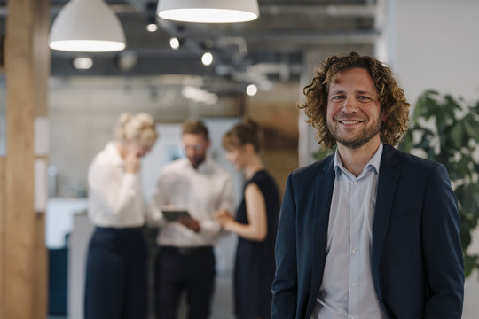 Portrait of confident businessman in office with colleagues in background