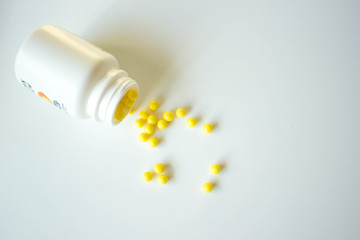 Vitamin C spilled from a white jar on a white blurred background. Yellow pills, vitamins.