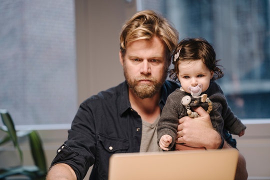 Casual businessman with daughter using laptop in office