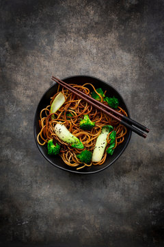Overhead view of bowl of soba noodles with pak choi and broccoli, soy sauce and black sesame