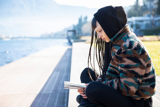 Young woman sitting on bench reading a book at Lake Como, Como, Italy