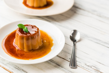 Close up of a flan creme caramel pudding with mint, a custard dessert against white wooden background
