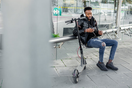 Man with smartphone and e-scooter at bus stop