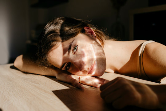 Portrait of young woman leaning on wooden table at sunlight