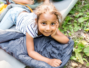 Little girl lying on sleeping bag, looking at camera