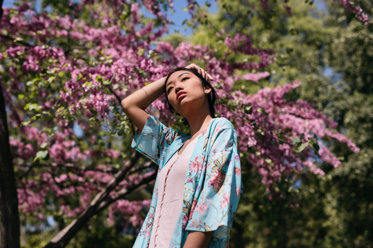 Beautiful young woman with blooming cherry tree in a public garden in spring