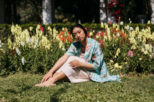 Beautiful young woman sitting in grass surrounded by flowers in a public garden in spring