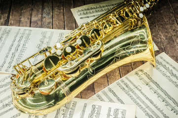 part of the case tube with pockets and bells of a yellow saxophone and letters with sheet music on an old wooden surface