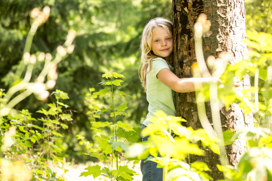 Little girl hugging tree in forest
