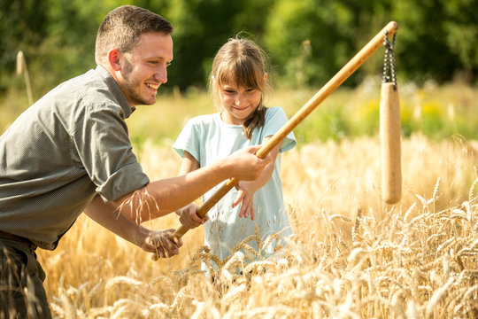 Children learning how to flail wheat in field
