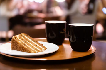 Close-up Two Coffee cups and plate with carrot cake or pie on round tray on table in cafe in the evening or at night.