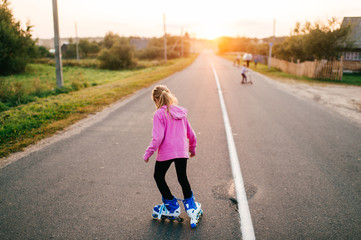 Pretty young girl in pink hoody roller-skates on the village road in the evening