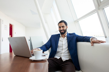 Fototapeta premium young successful businessman use a laptop and drink coffee in the morning at work, a freelancer is sitting with a computer in a white cafe