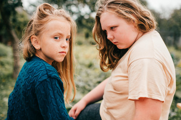 Portrait of young lovely girl with her elder chubby sister lie on the coverlet in the garden and smile