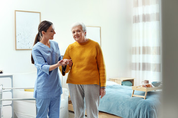 Fototapeta premium Care worker helping elderly woman to walk in geriatric hospice