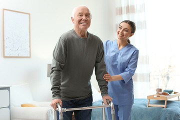 Care worker helping elderly man with walker in geriatric hospice - obrazy, fototapety, plakaty
