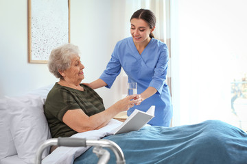 Care worker giving water to elderly woman in geriatric hospice