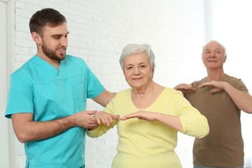 Fototapeta premium Care worker helping elderly woman to do sports exercise in hospital gym.