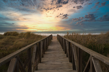 Wooden path and sunset on the beach of El Palmar, near the Caños de Meca, an ideal place to spend a great holiday on the coast of the province of Cadiz, in Andalusia, Spain - obrazy, fototapety, plakaty