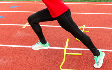 Obraz premium Sprinter performing running drill over yellow mini hurdle on a track
