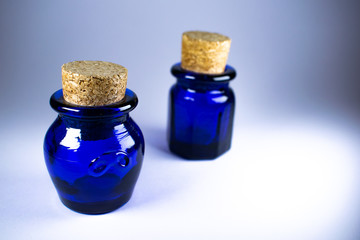 Two blue bottles with corks, oval and hexagonal bottle, white background some shadows, one focused...