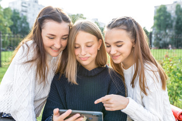 Three teenage girls of 12-14 years old, summer city watching videos phone, happy smiling people having fun rejoice. Social networks Internet, application smartphone. Casual clothes, warm sweaters.