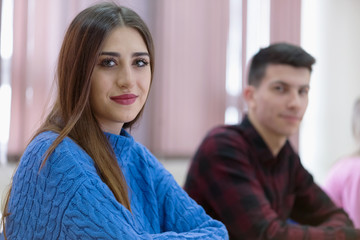 Group of  university IT technologies students working on practice lessons. Sitting near therir computer and looking for solution during class. Female student smiling into camera.