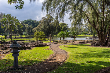 Hilo, Hawaii, USA. - January 9, 2012: Path winding through green lawn among trees with Japanese lanterns on side in Liliuokalani Gardens. Sunshine but cloudscape.