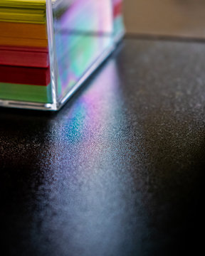 Posting notes rack gives reflections from the sun that looks like a tiny rainbow, colorful papers, reclections, acrylic box, sticky notes, work desk in office